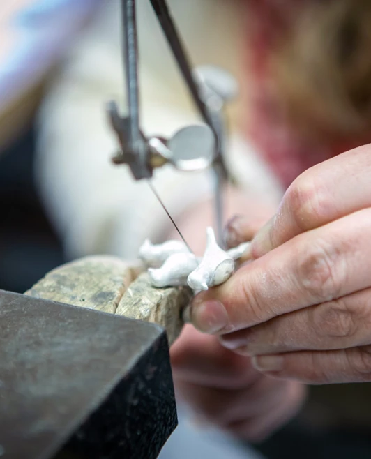 A close-up of a jeweller using a precision saw to cut through a silver piece in a workshop environment. A close-up of a jeweller using a precision saw to cut through a silver piece in a workshop environment.